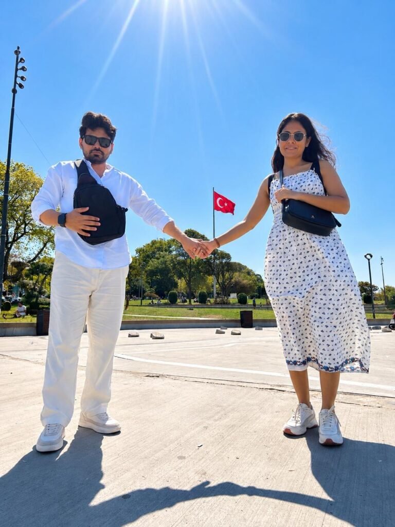 Tushar and Sanju holding hands in Istanbul with a Turkish flag behind them